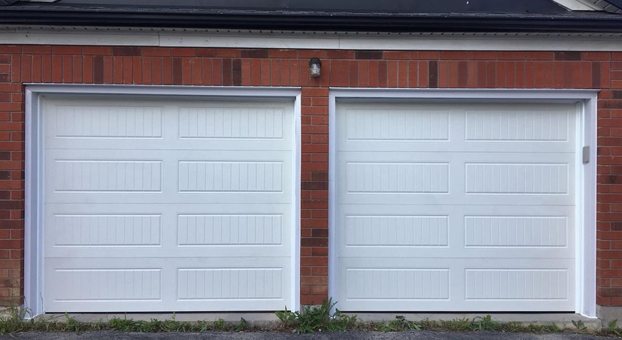 White raised panel garage doors installed in a brick home